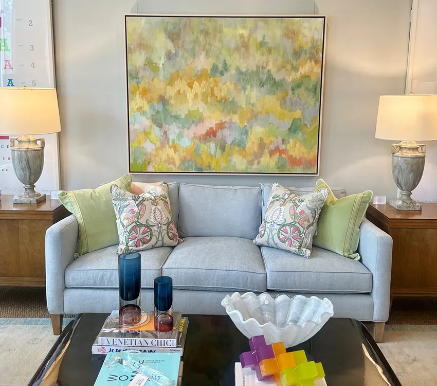 Painting of yellows and greens hanging above blue sofa
